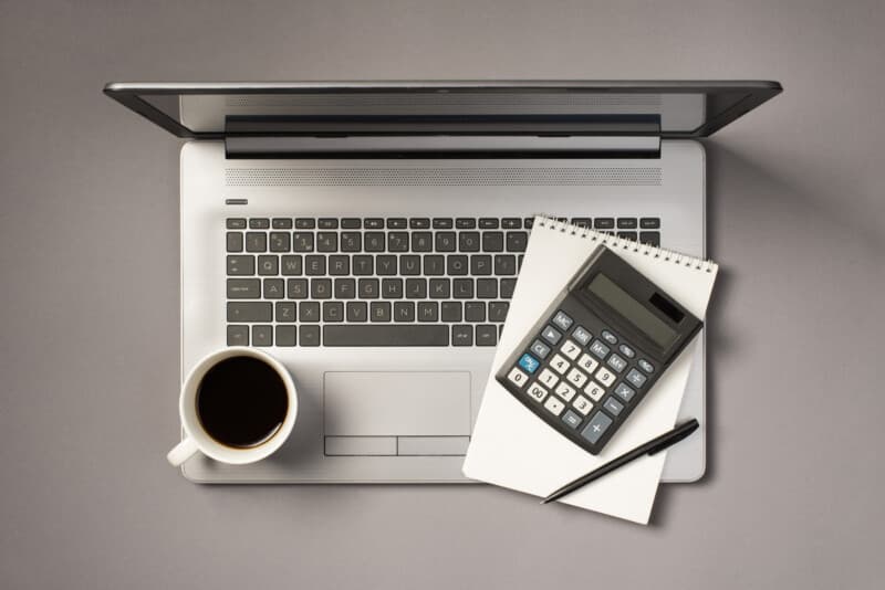 Top view photo of cup of drink calculator pen and notebook on grey laptop on isolated grey background