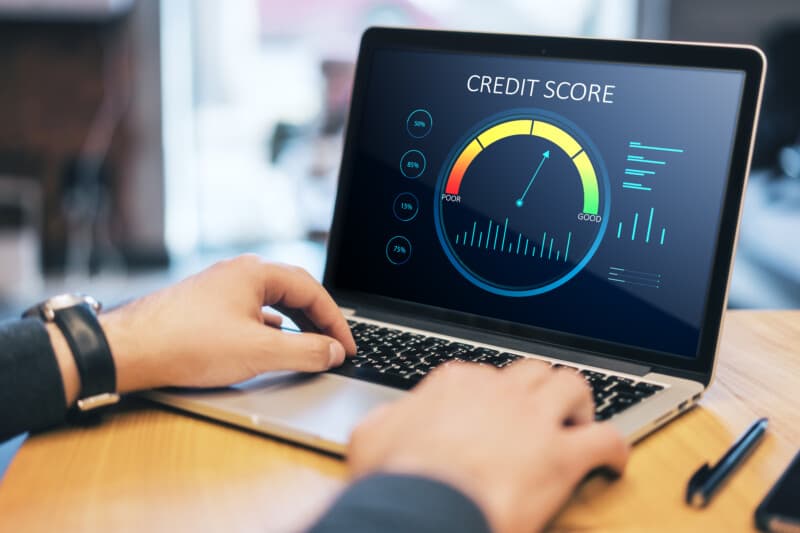 Close up of hands at wooden desktop with laptop computer and abstract credit score scale on screen.