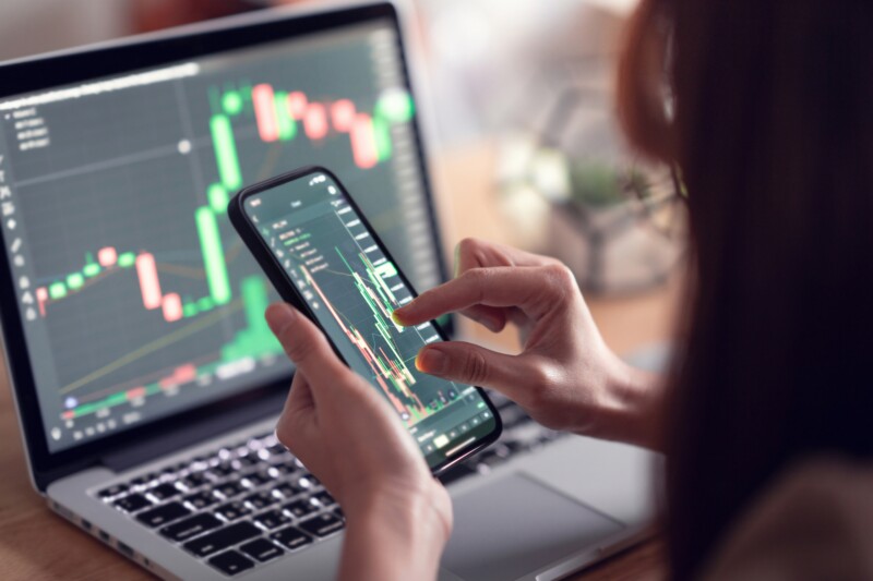 Woman checking Bitcoin trading chart on a phone and laptop screen