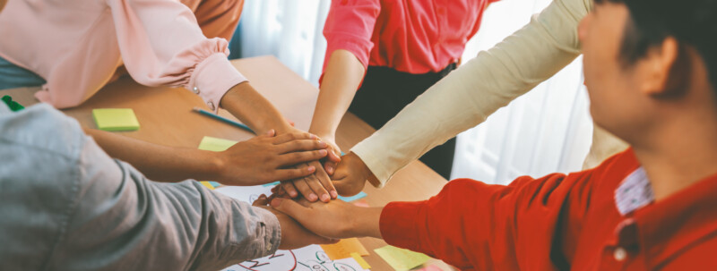 Business people putting their hands together at meeting room. Variegated.